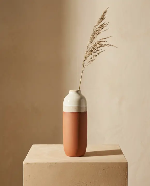 Terracotta bud vase with a cream glaze band holding a dried grass stem